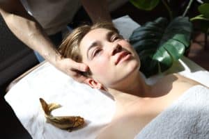 Woman lying on a massage table wrapped in a towel, receiving a head massage from above