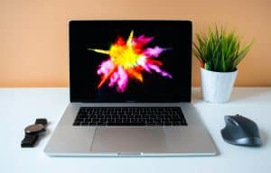 Modern design studio desk viewed front-on, with laptop, watch, small succulent, and screen showing colourful abstract artwork