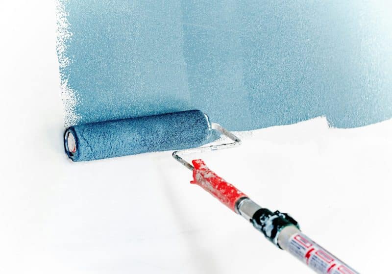 Close-up of a paint roller applying blue paint over a white wall