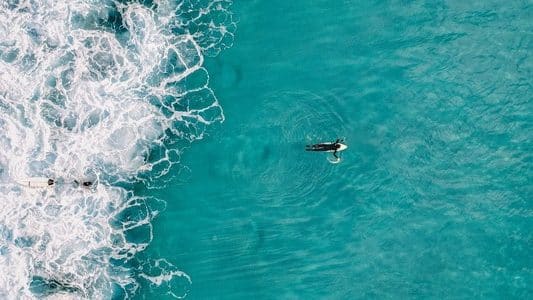 Aerial drone shot of a surfer paddling out past whitewater on the Sunshine Coast